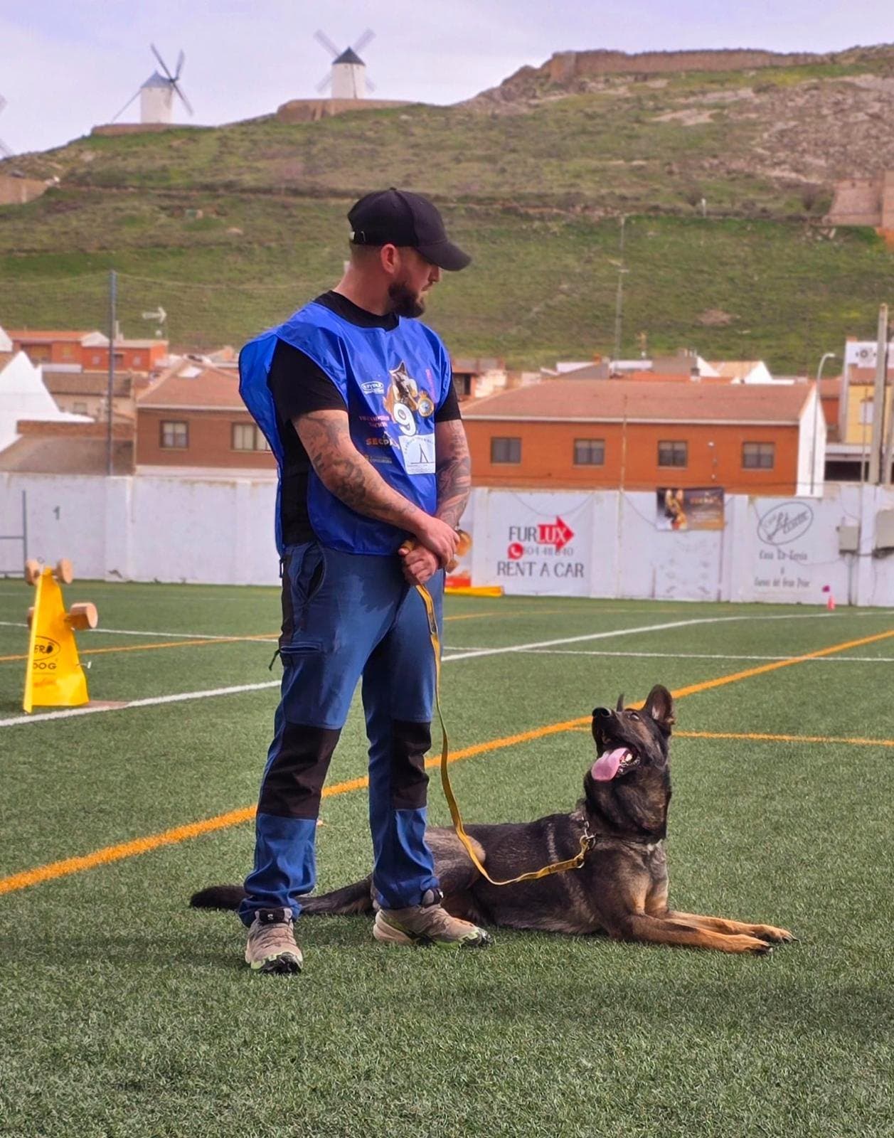 Nando Cañero y Xena en la pista de obediencia del Campeonato Nacional IGP con los molinos de Consuegra al fondo